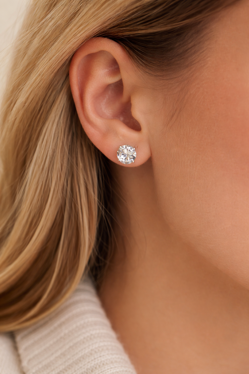 Close-up of a person wearing a diamond stud earring with a neutral background